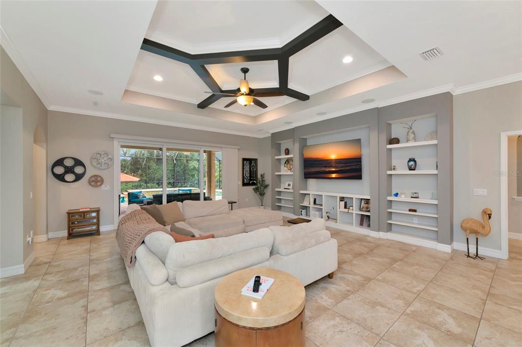 A living room features a tray ceiling with dark beams, a sectional sofa, and built-in shelving — 15208 21ST AVENUE E, BRADENTON, FL