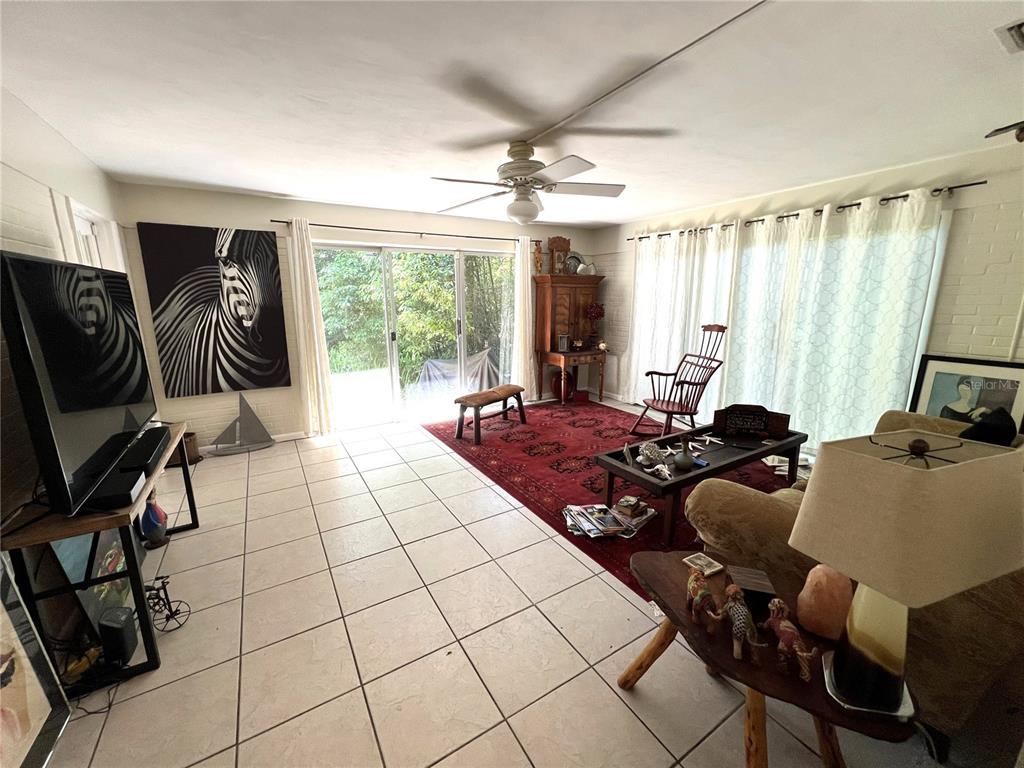 A living room features white tile floors, a large red rug, sliding glass doors, and furniture — 1617 NW 7TH PLACE, GAINESVILLE, FL