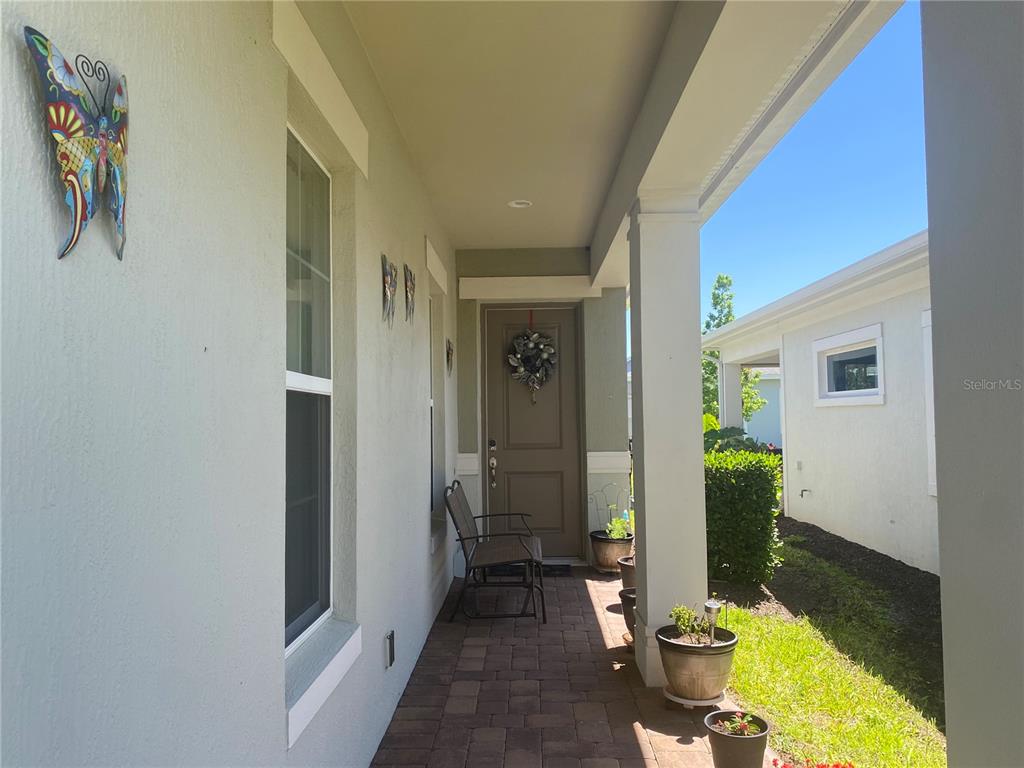 A covered front porch features a brick paver floor, a brown door, and potted plants — 2410 DATURA LOOP, ST CLOUD, FL