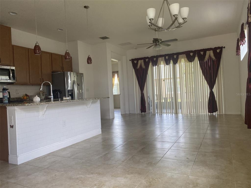 An open-concept kitchen with wood cabinets and a breakfast bar overlooks a tiled living area — 2410 DATURA LOOP, ST CLOUD, FL