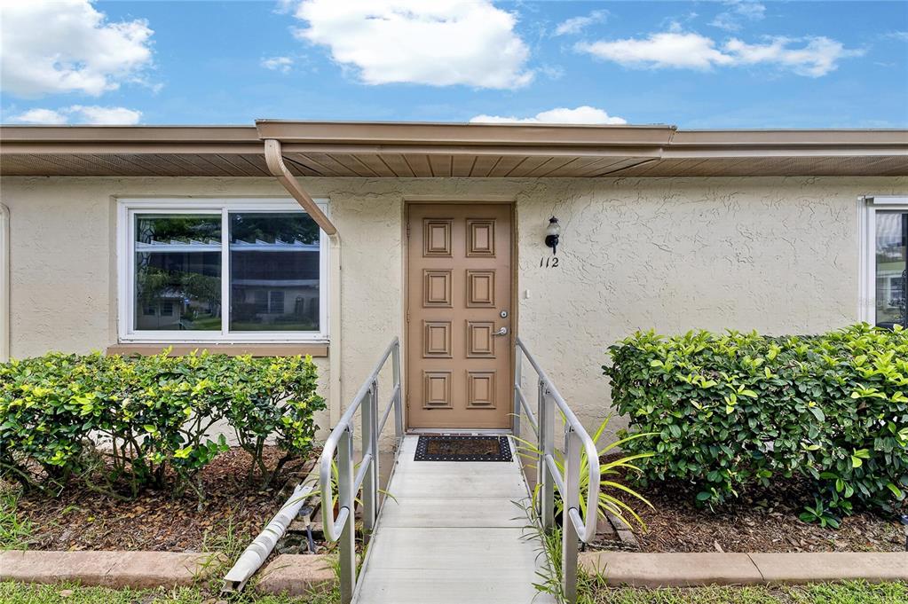 A tan exterior wall features a brown front door with a wheelchair ramp leading to it — 112 GLOUCESTER BOULEVARD UNIT 345, SUN CITY CENTER, FL
