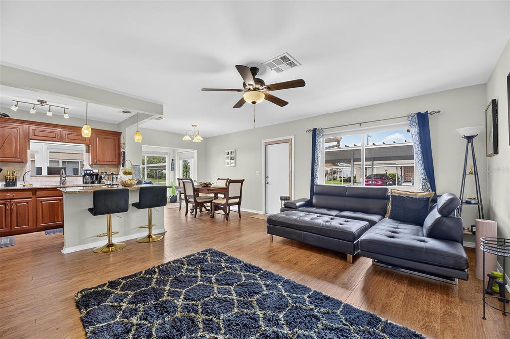 An open-concept living and dining area features wood-look flooring, a dark sectional, and kitchen cabinetry — 112 GLOUCESTER BOULEVARD UNIT 345, SUN CITY CENTER, FL