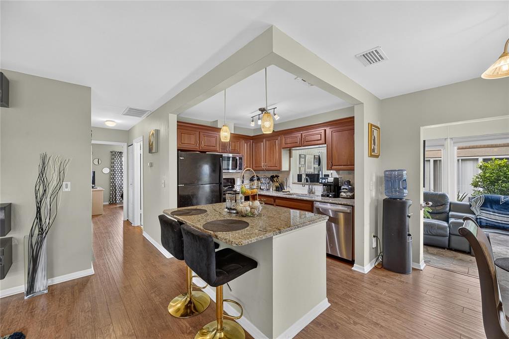 A kitchen features wood cabinets, granite countertops, a central island with bar stools, and appliances — 112 GLOUCESTER BOULEVARD UNIT 345, SUN CITY CENTER, FL