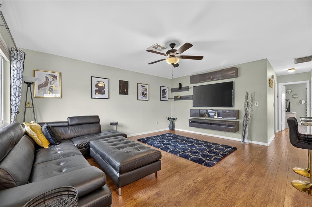 A living room features a black sectional sofa, a patterned rug, and a wall-mounted television — 112 GLOUCESTER BOULEVARD UNIT 345, SUN CITY CENTER, FL