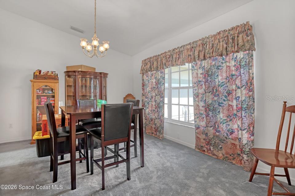 A dining room features gray carpeting, a dark wood table with chairs, and floral curtains — 3975 TANGLE DRIVE, TITUSVILLE, FL