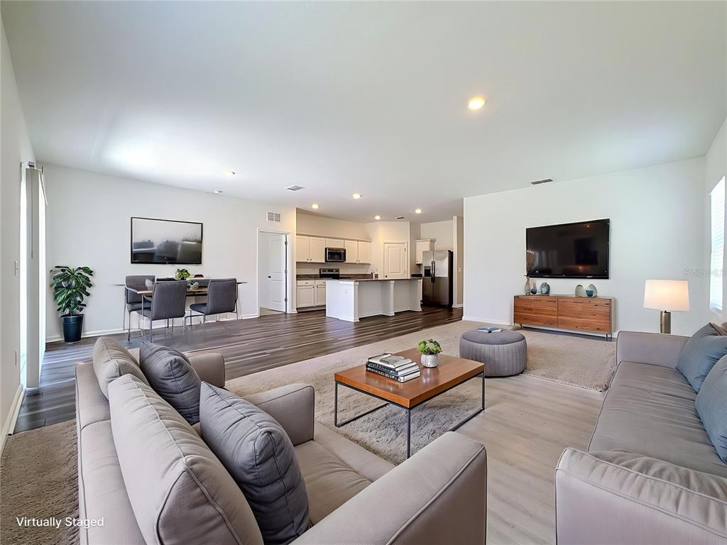 An open-concept living and dining area features wood-look flooring, a kitchen island, and neutral furniture — 1349 ANCHOR BEND DRIVE, RUSKIN, FL