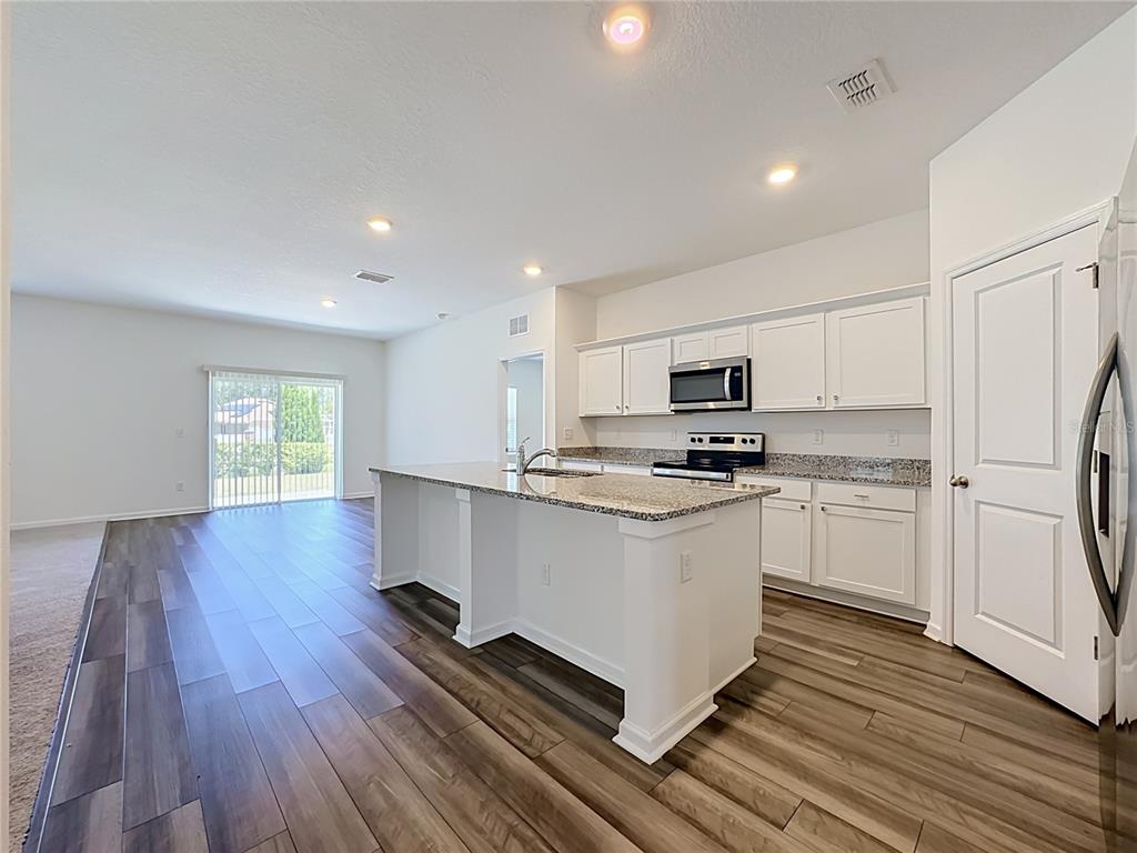 A kitchen with white cabinets, granite countertops, and an island opens to a living area — 1349 ANCHOR BEND DRIVE, RUSKIN, FL