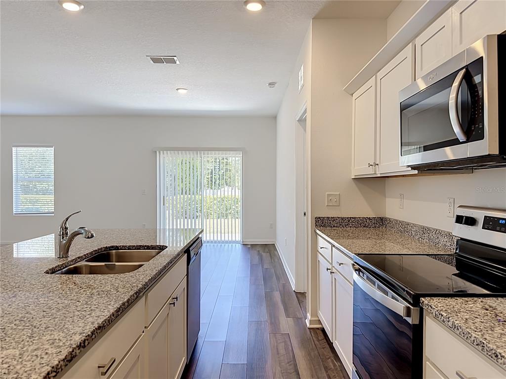 A kitchen with white cabinets, granite countertops, and stainless steel appliances overlooks a living area — 1349 ANCHOR BEND DRIVE, RUSKIN, FL