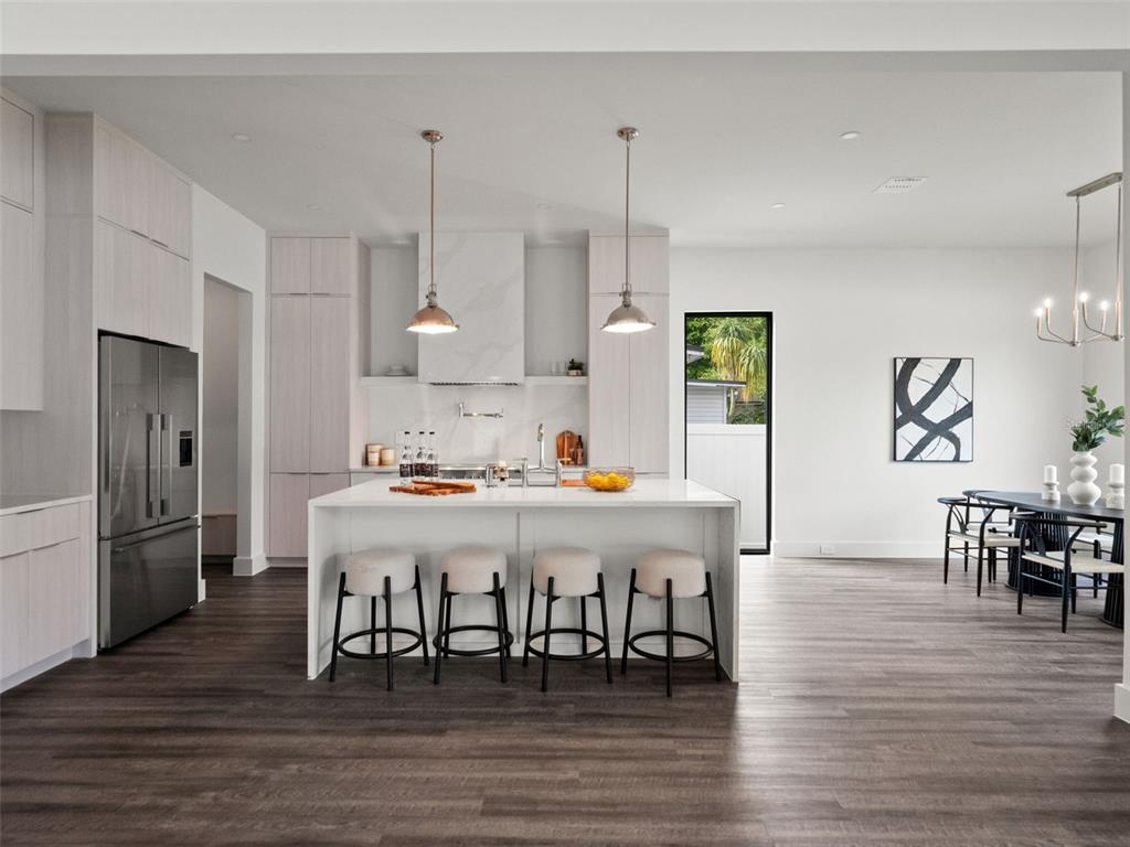 A modern kitchen features light wood cabinetry, a white island with four stools, and dark flooring — 1320 CLOVERLAWN AVENUE, ORLANDO, FL