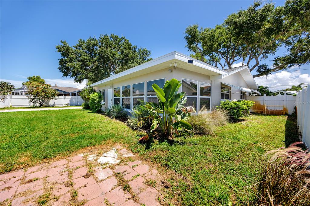 The exterior of a single-story house features a paved patio, large windows, and landscaping — 1744 HARBOR CIRCLE E, LARGO, FL