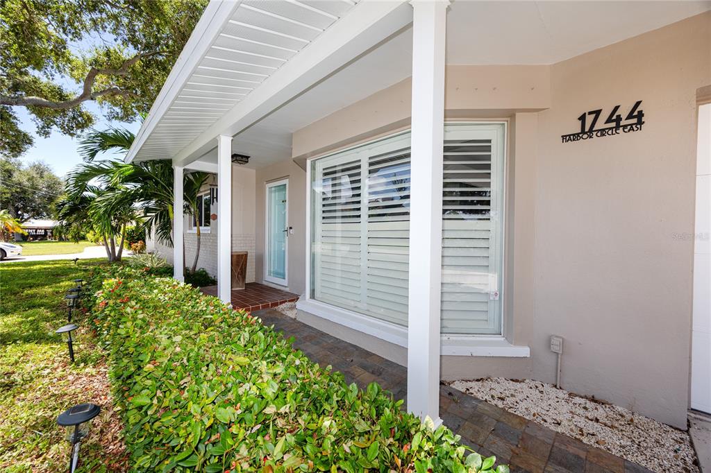 A covered porch features a large window with white shutters and a tiled entryway — 1744 HARBOR CIRCLE E, LARGO, FL