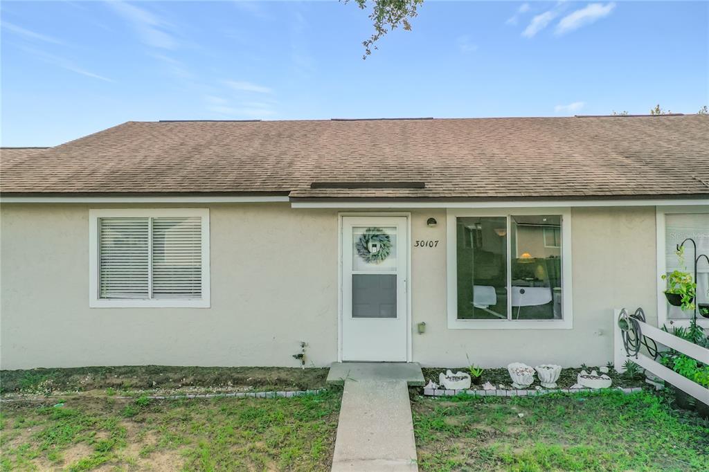 A single-story house exterior features a beige stucco facade, a brown shingled roof, and a walkway — 30107 TAVARES RIDGE BOULEVARD UNIT 30107, TAVARES, FL