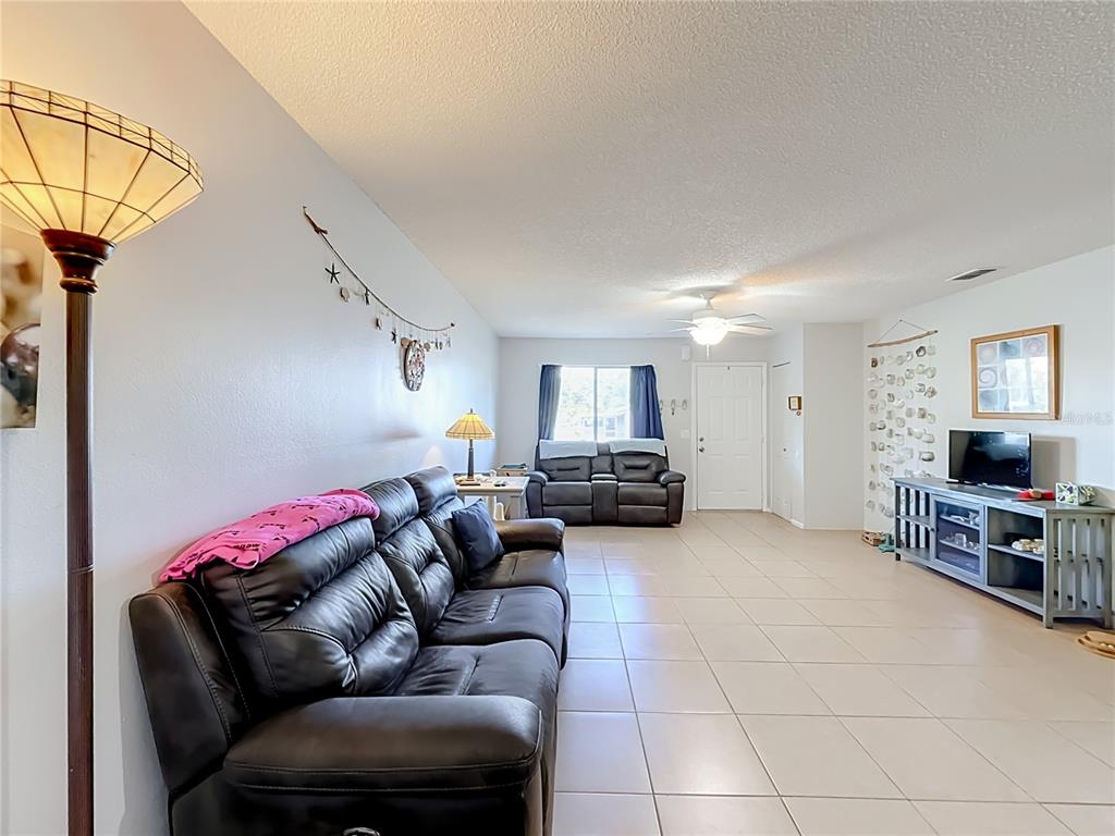 A living room features tile flooring, two dark leather sofas, and a television on a stand — 30107 TAVARES RIDGE BOULEVARD UNIT 30107, TAVARES, FL