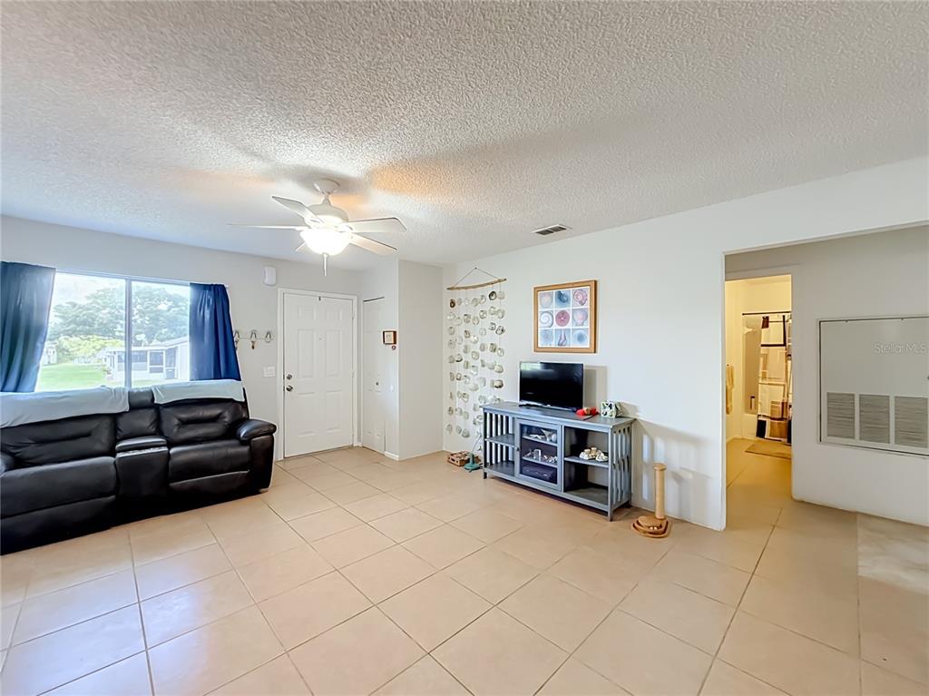 A living room features beige tile flooring, a dark leather sofa, and a television console — 30107 TAVARES RIDGE BOULEVARD UNIT 30107, TAVARES, FL