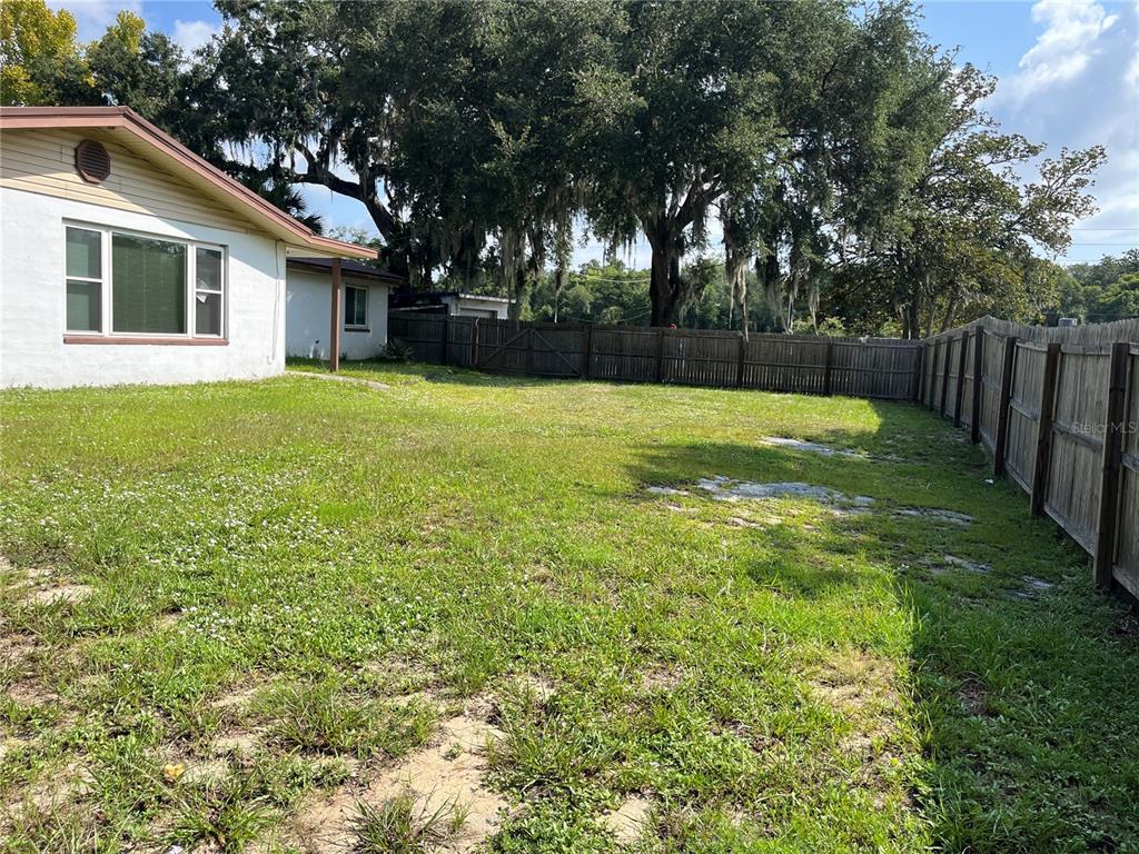 A grassy backyard features a white house, a wooden fence, and large oak trees — 900 N US HIGHWAY 1, ORMOND BEACH, FL