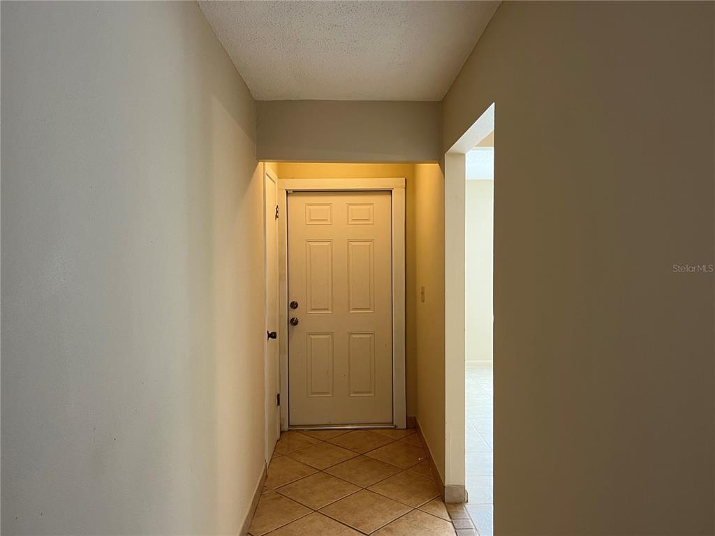 A hallway with beige walls and tile flooring leads to a white six-panel front door — 900 N US HIGHWAY 1, ORMOND BEACH, FL