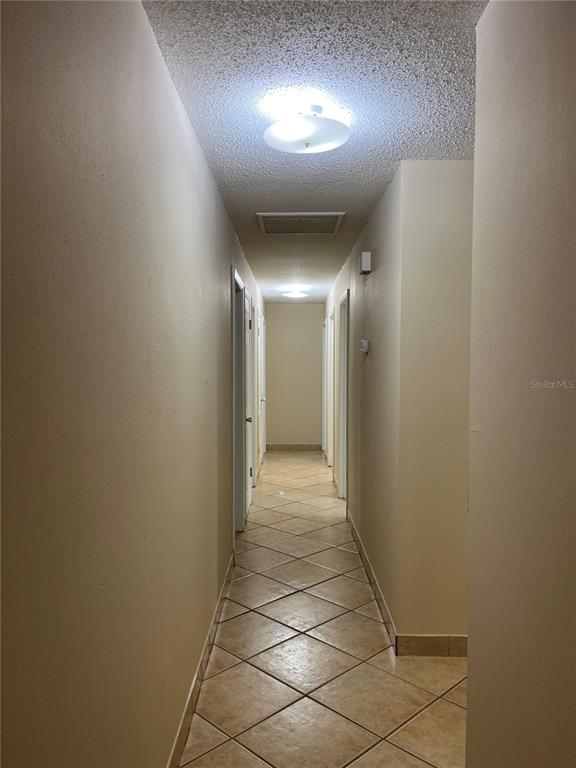 A long hallway features beige walls, a popcorn ceiling, and light-colored diagonal floor tiles — 900 N US HIGHWAY 1, ORMOND BEACH, FL
