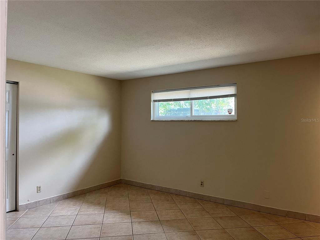 An empty bedroom features beige walls, a single window, and light-colored diagonal floor tiles — 900 N US HIGHWAY 1, ORMOND BEACH, FL