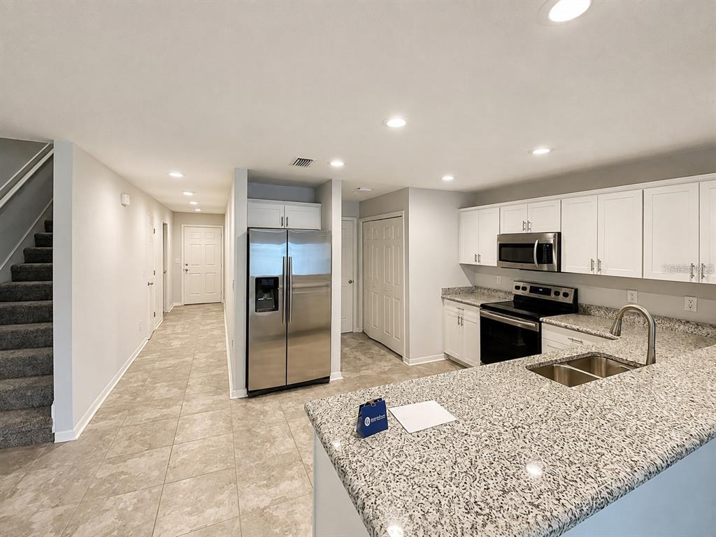 A kitchen with white cabinets, granite countertops, stainless steel appliances, and tile flooring — 7306 MERLOT SIENNA AVENUE, GIBSONTON, FL