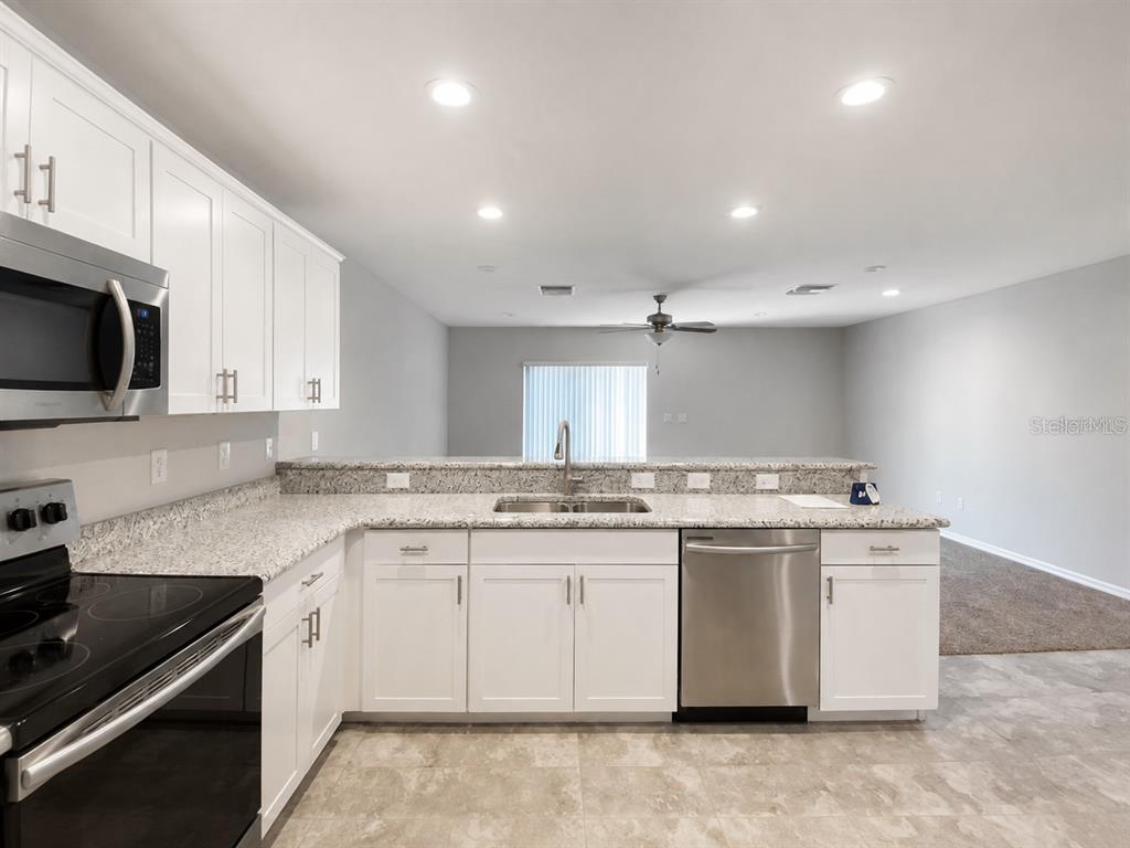 A kitchen with white cabinets, granite countertops, and stainless steel appliances overlooks a living area — 7306 MERLOT SIENNA AVENUE, GIBSONTON, FL