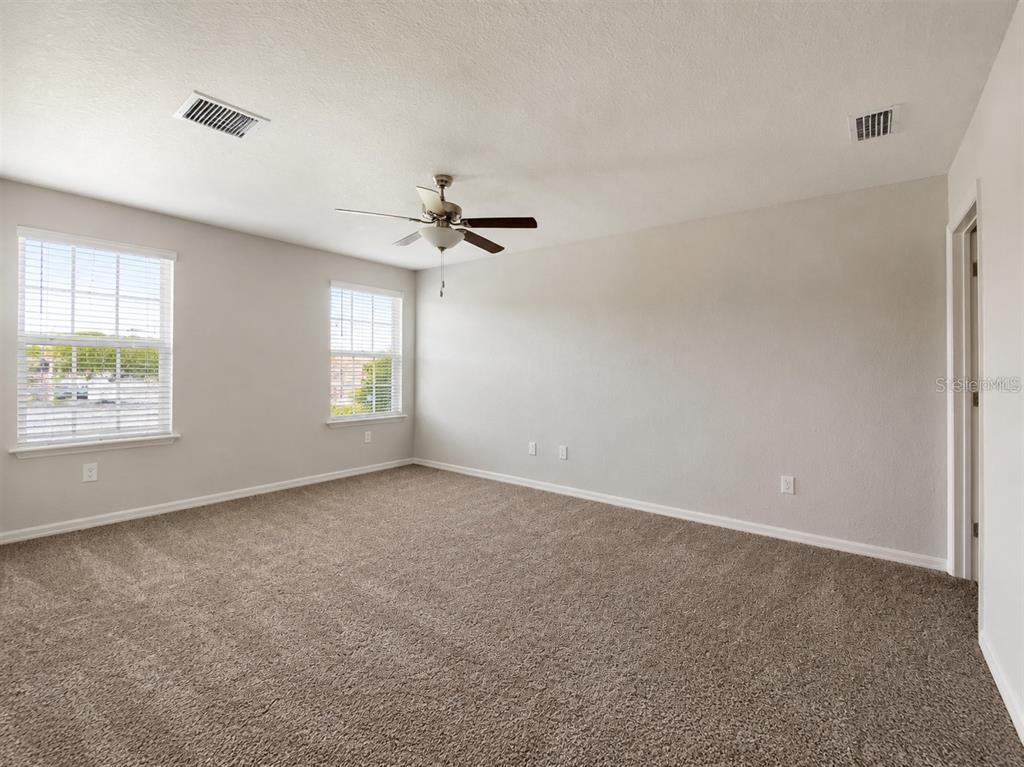 An empty bedroom features beige carpet, light gray walls, two windows, and a ceiling fan — 7306 MERLOT SIENNA AVENUE, GIBSONTON, FL
