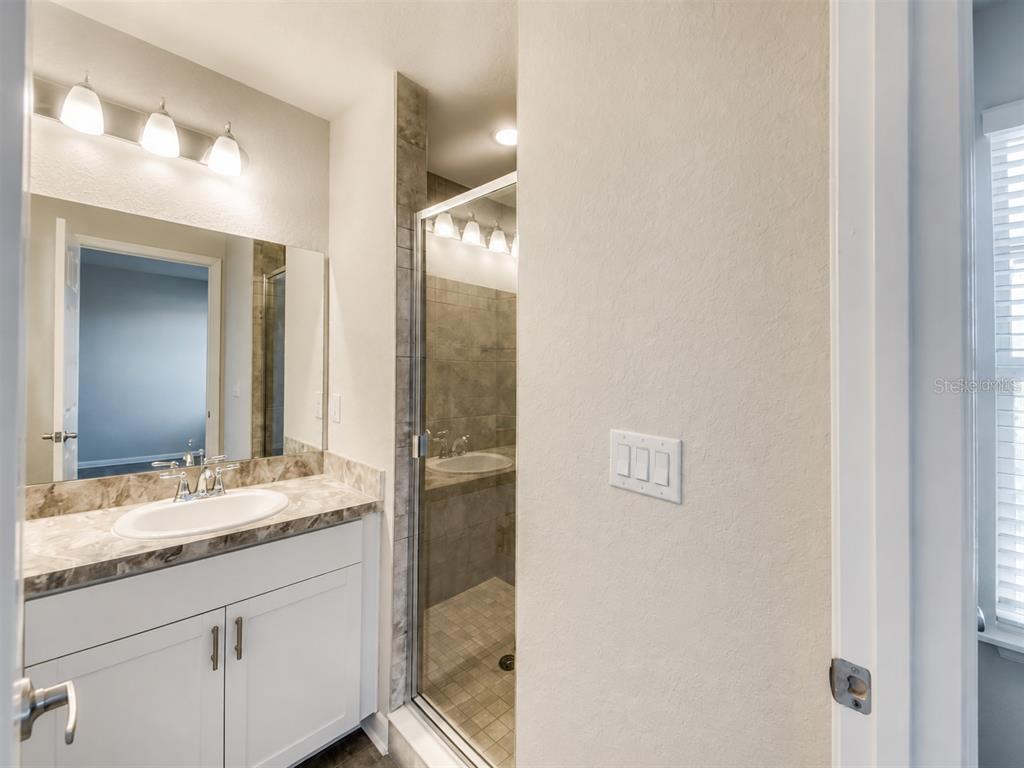 A bathroom features a white vanity with a marble countertop, a mirror, and a glass-enclosed shower — 7306 MERLOT SIENNA AVENUE, GIBSONTON, FL