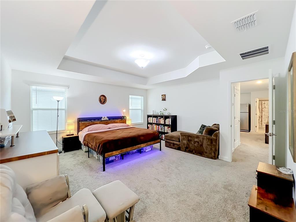 A spacious bedroom features a tray ceiling, carpeted flooring, a bed with under-lighting, and furniture — 11835 BOLDFACE DRIVE, ORLANDO, FL