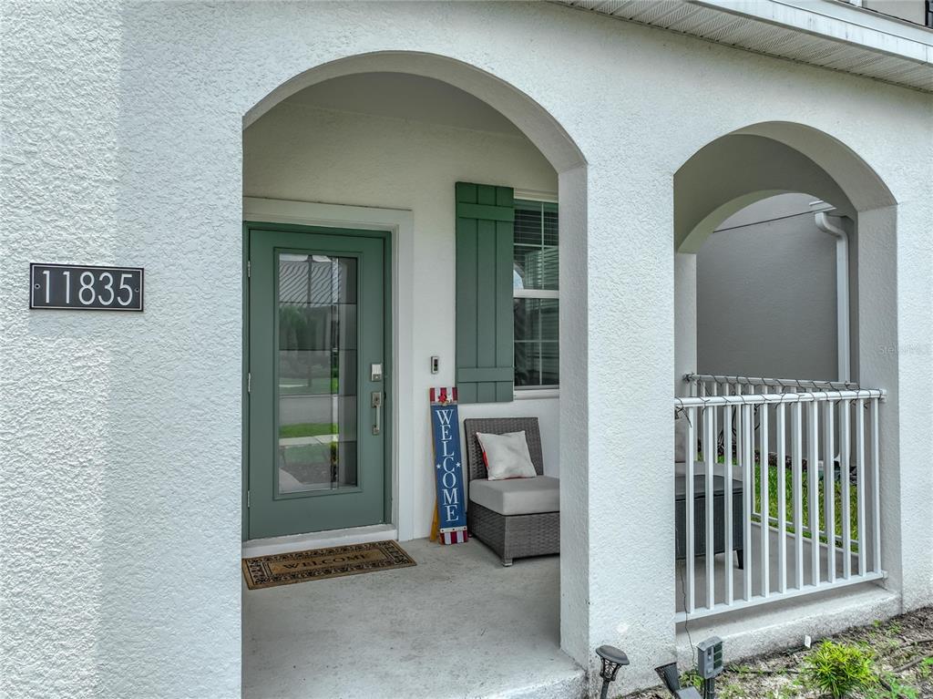A covered entryway features a green front door, a welcome sign, and a small patio chair — 11835 BOLDFACE DRIVE, ORLANDO, FL