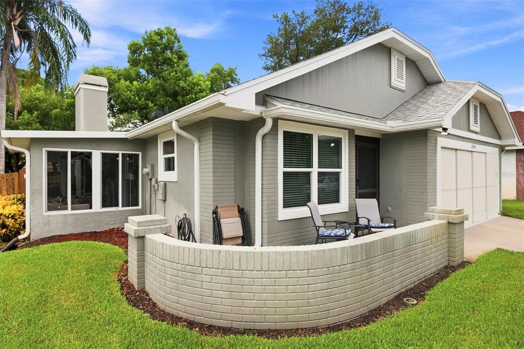 A single-story gray brick house features a curved front patio wall and a garage — 2234 SPRINGFLOWER DR., CLEARWATER, FL