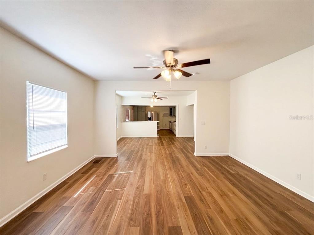 An empty living room with wood-look flooring leads into a kitchen with a breakfast bar — 320 W BULLARD AVENUE, LAKE WALES, FL