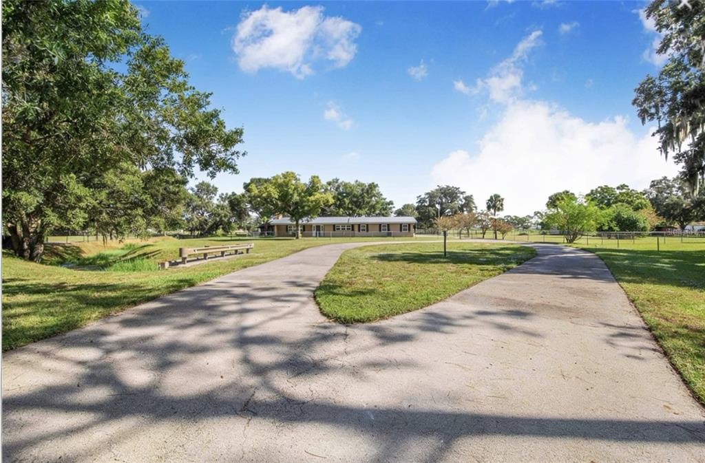 A paved circular driveway leads to a single-story house surrounded by trees and green lawn — 4854 E HINSON AVENUE, HAINES CITY, FL