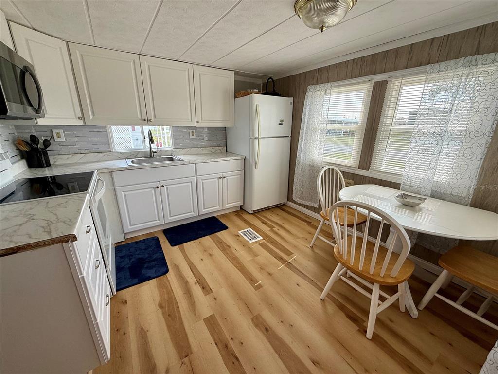 A kitchen features white cabinets, a white refrigerator, a dining table, and wood-look flooring — 1360 IBIS DRIVE, ENGLEWOOD, FL