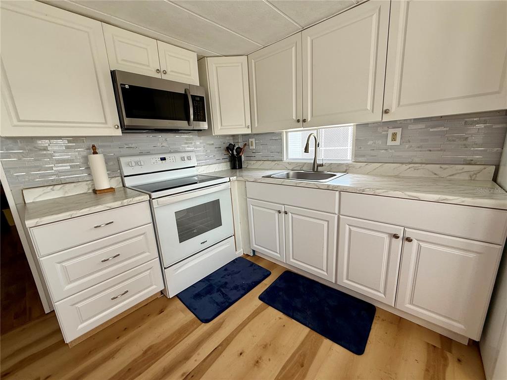 A kitchen with white cabinets, stainless steel appliances, a marble-look countertop, and light wood flooring — 1360 IBIS DRIVE, ENGLEWOOD, FL