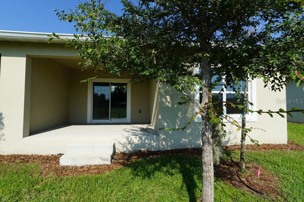 A covered concrete patio with a sliding glass door sits beside a window and tree — 2936 SUNRIDGE LOOP, ST CLOUD, FL