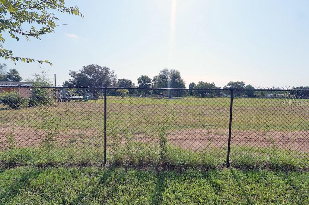 A chain-link fence borders a large, flat, grassy lot under a bright, clear sky — 2936 SUNRIDGE LOOP, ST CLOUD, FL