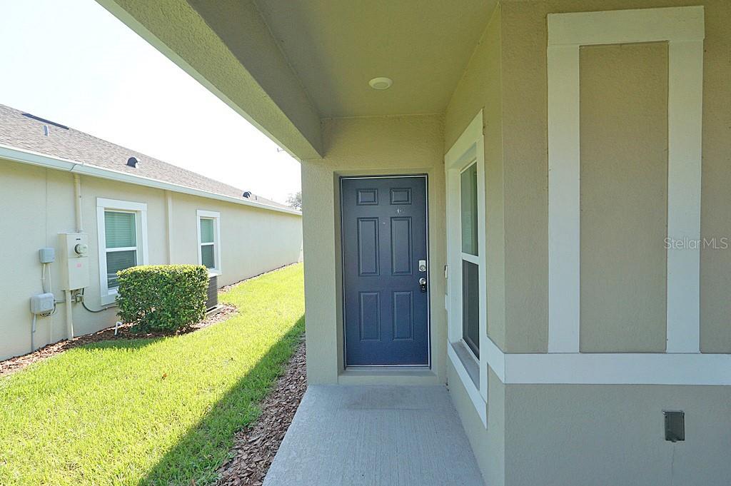 A covered entryway features a blue front door and a concrete porch next to grass — 2936 SUNRIDGE LOOP, ST CLOUD, FL