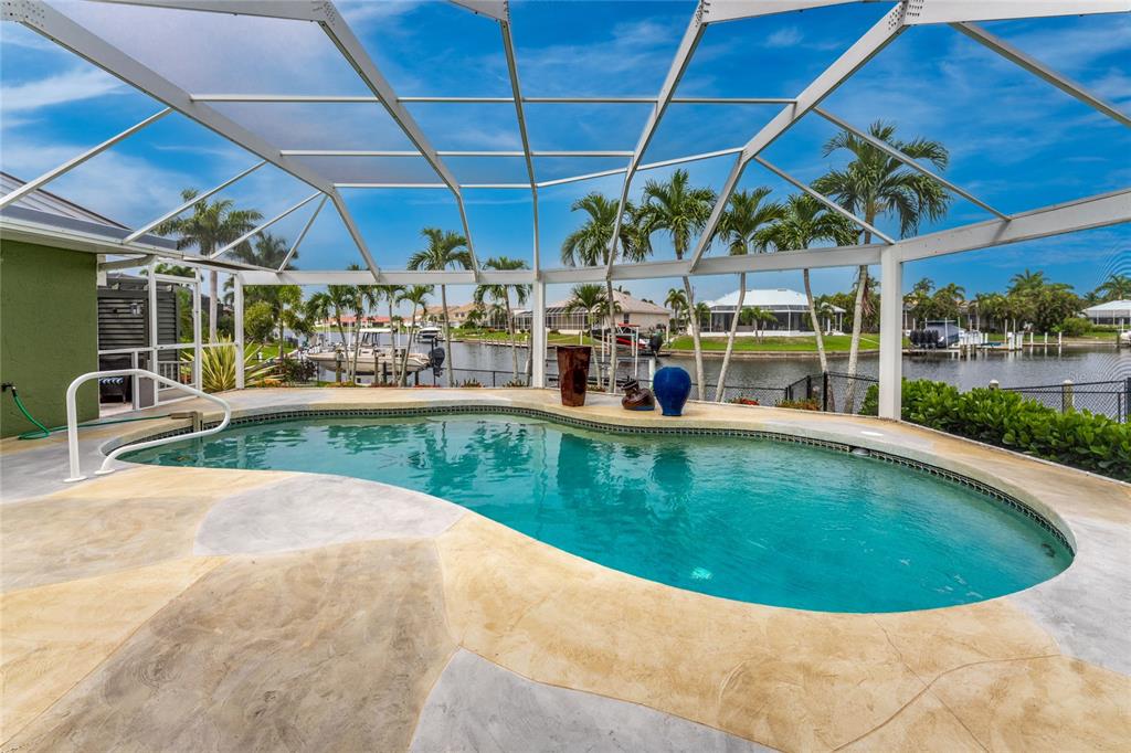 A swimming pool with a screened enclosure overlooks a canal with boats and palm trees — 3601 WHIPPOORWILL BOULEVARD, PUNTA GORDA, FL