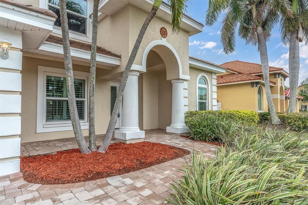 The exterior of a tan house features a covered entryway with white columns and palm trees — 906 LANDMARK CIRCLE S, TIERRA VERDE, FL