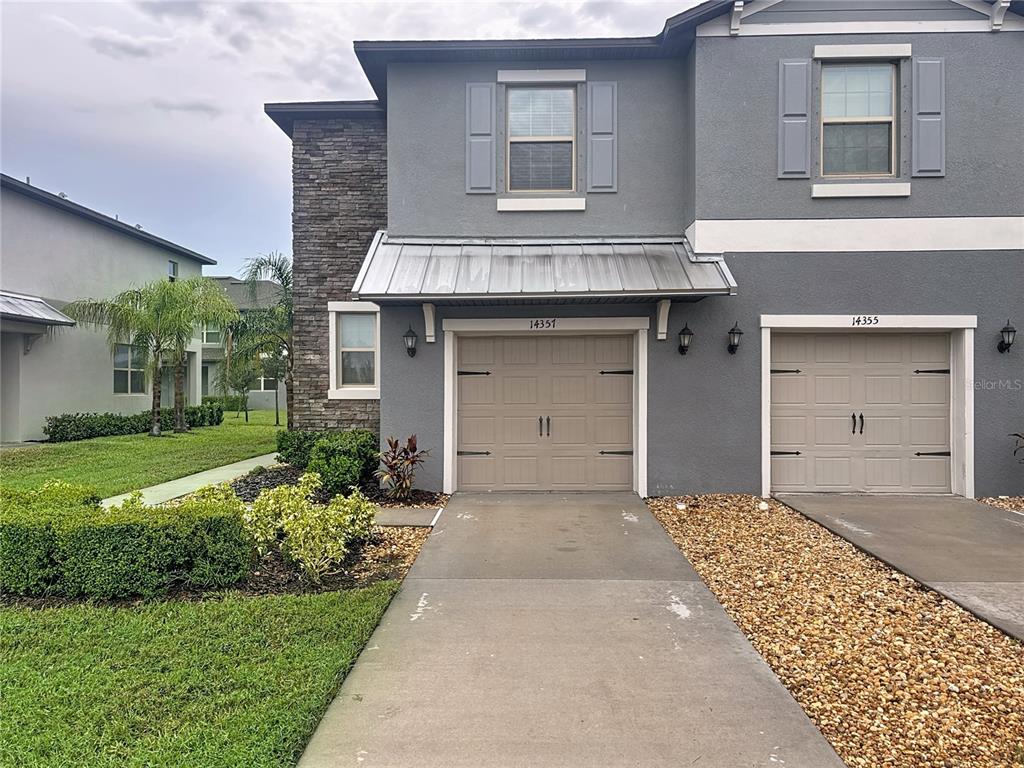 A two-story gray townhouse exterior features a stone accent wall and two beige garage doors — 14357 EASY GOER STREET, SUN CITY CENTER, FL