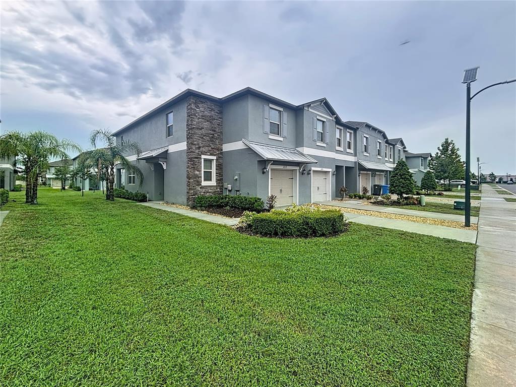 A two-story townhouse exterior with a gray stucco facade, stone accents, and an attached garage — 14357 EASY GOER STREET, SUN CITY CENTER, FL