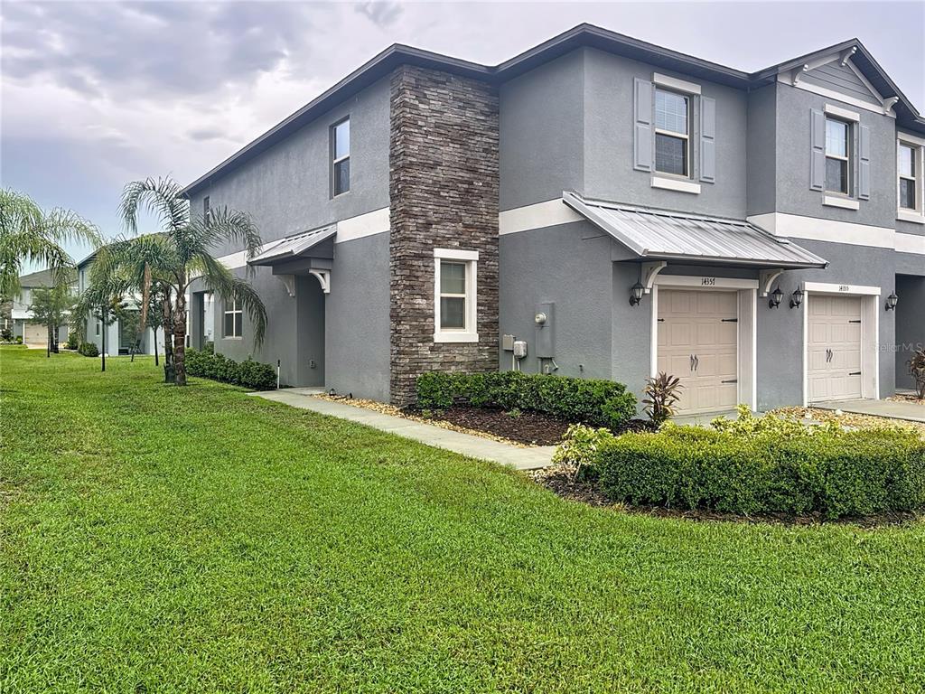 A two-story gray townhouse with a stone accent wall, metal roof awnings, and a garage — 14357 EASY GOER STREET, SUN CITY CENTER, FL