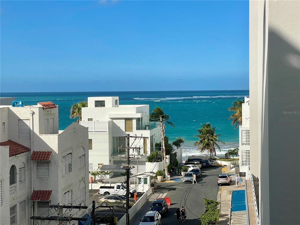 An elevated view overlooks a coastal street with white buildings, parked cars, and the ocean — 1124 ASHFORD AVENUE UNIT 6A, SAN JUAN, PR