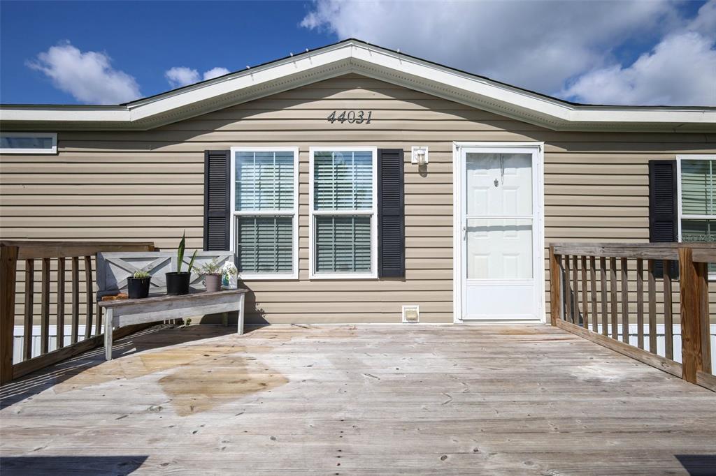A wooden deck leads to the front door of a tan house with vinyl siding — 44031 EAST ROAD, PAISLEY, FL