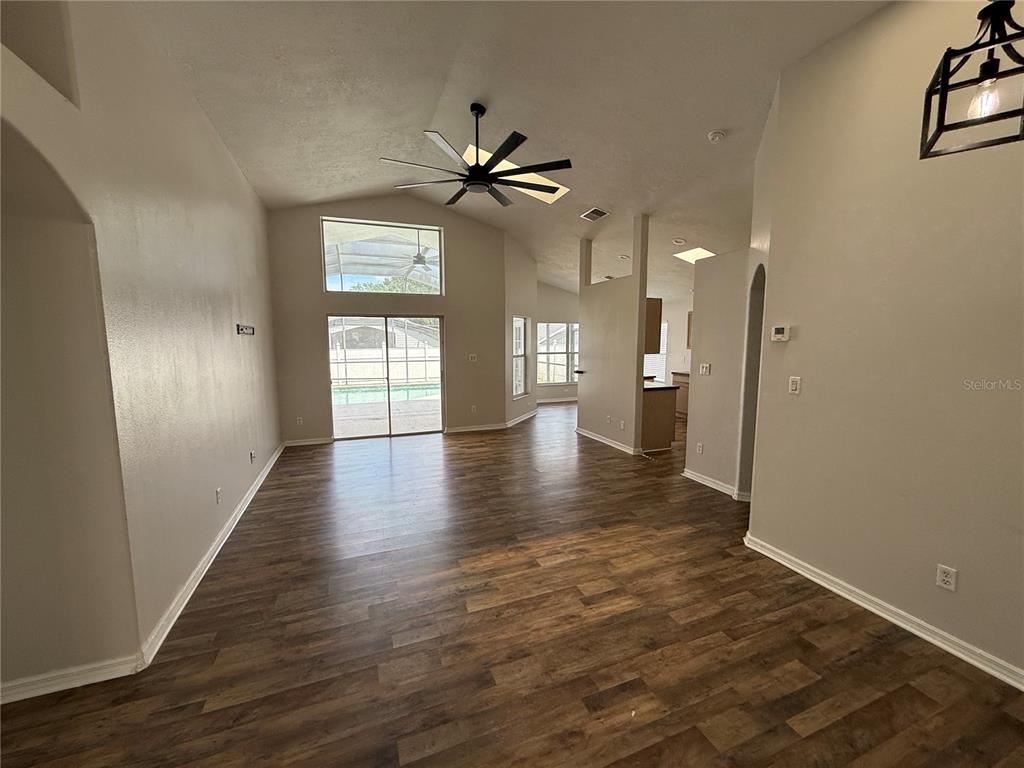 An open-concept living area features wood-look flooring, vaulted ceilings, and sliding glass doors to a pool — 16049 MAGNOLIA HILL STREET, CLERMONT, FL