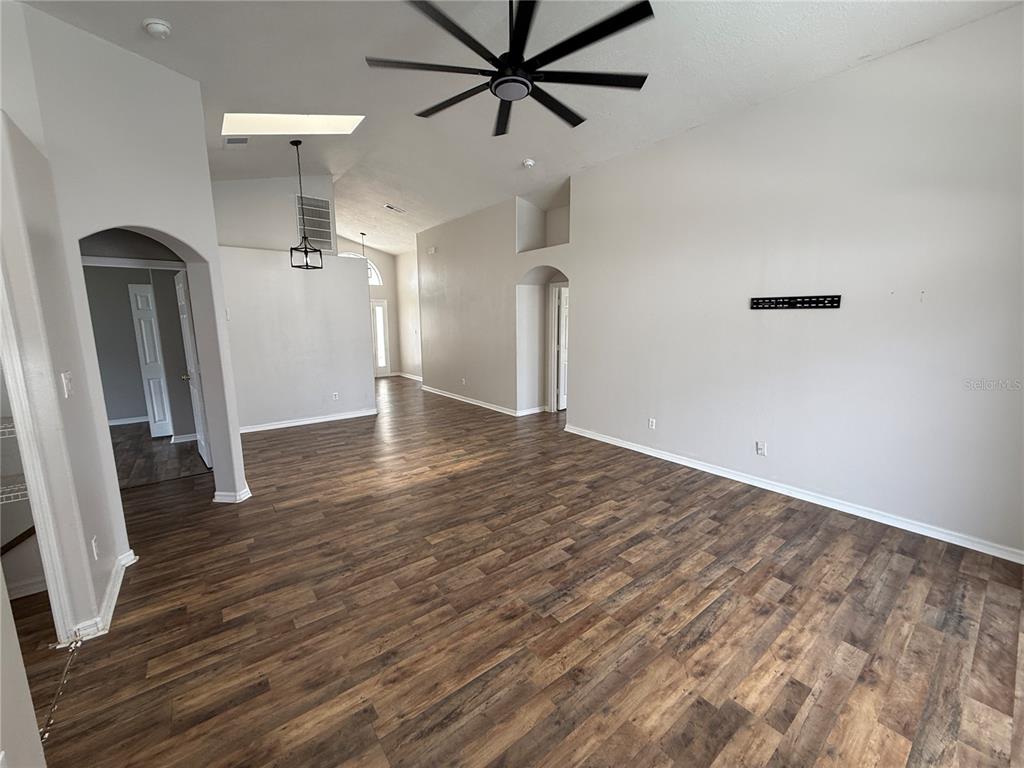 An open-concept living area features vaulted ceilings, a ceiling fan, and wood-look flooring — 16049 MAGNOLIA HILL STREET, CLERMONT, FL