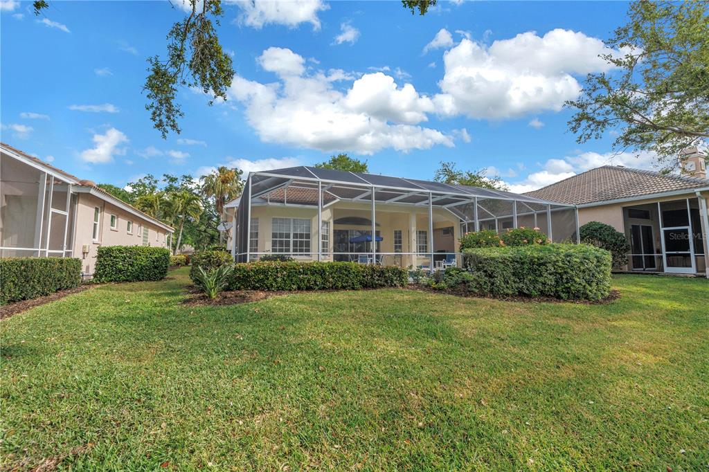 A backyard view of a house with a screened-in pool enclosure and manicured landscaping — 4334 MIRABELLA CIRCLE, BRADENTON, FL