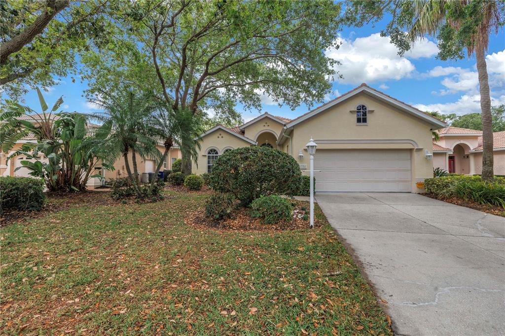 A single-story house with a beige stucco exterior, a two-car garage, and a landscaped yard — 4334 MIRABELLA CIRCLE, BRADENTON, FL