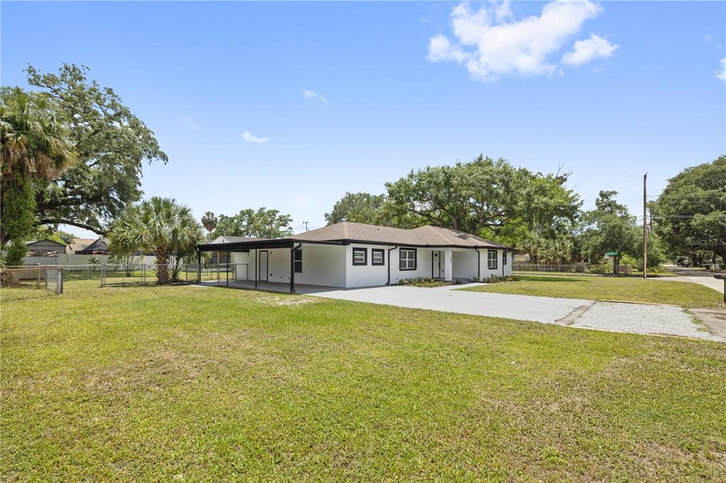 A white, single-story house with a black roof and carport sits on a grassy lot — 408 W VIRGINIA AVENUE, TAMPA, FL