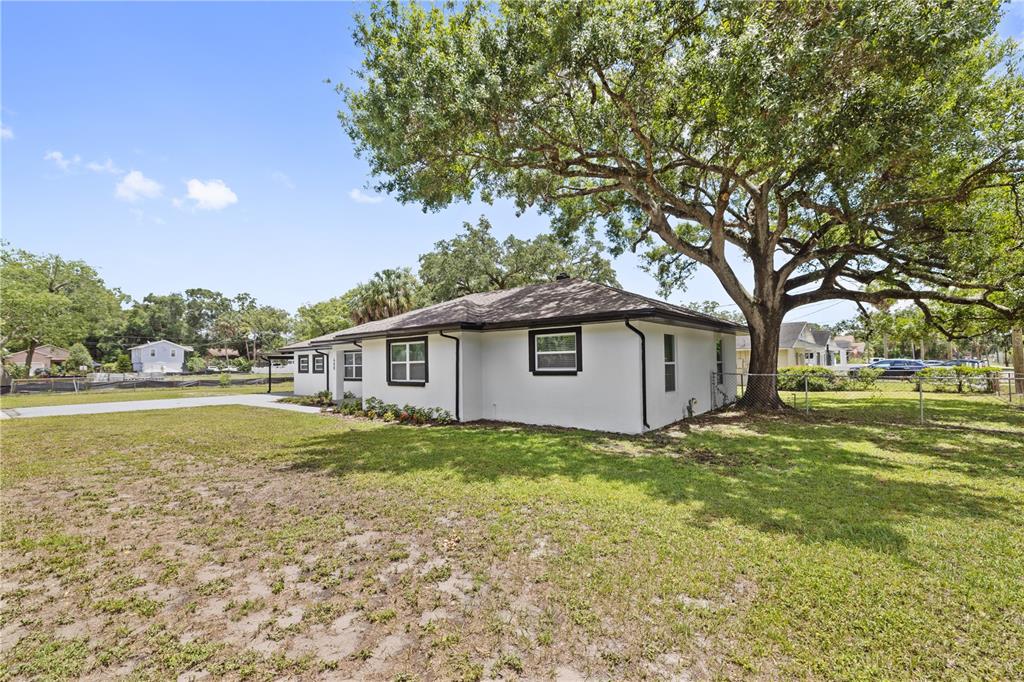 A white single-story house with dark trim sits on a grassy lot under a large tree — 408 W VIRGINIA AVENUE, TAMPA, FL