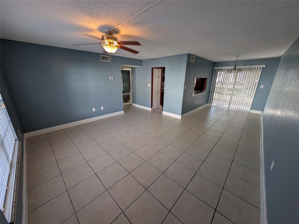 An empty living room features blue walls, tile flooring, a ceiling fan, and sliding glass doors — 2564 SE 15TH AVENUE UNIT E, OCALA, FL